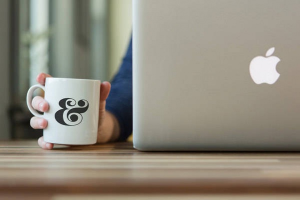 Free PSD Photorealistic In Hand Coffee Cup Mockup with Apple Macbook Pro